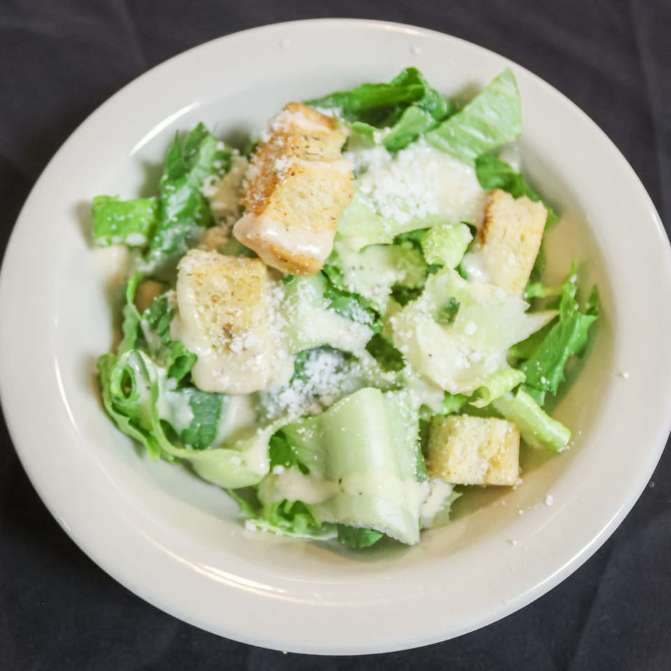 A Caesar salad with romaine lettuce, croutons, and parmesan cheese in a white bowl.