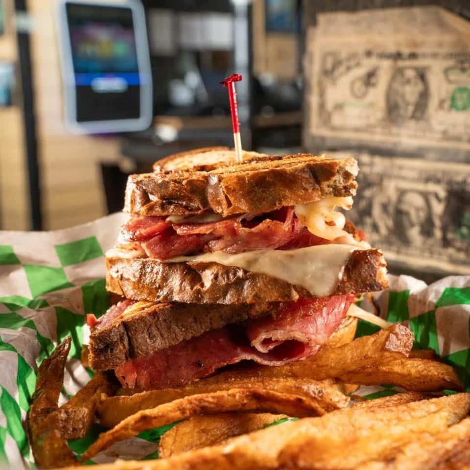 A stacked Reuben sandwich with fries in a green and white checkered basket at The Wexford Irish Pub & Grille.