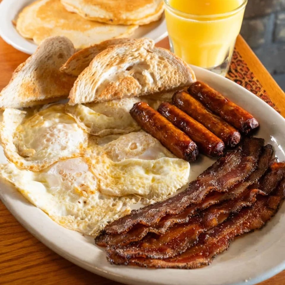 A full Irish breakfast with fried eggs, bacon, sausages, toast, pancakes, and orange juice.
