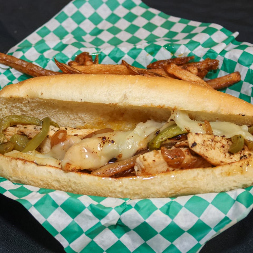 Chicken cheesesteak with green peppers, onions, and fries in a green and white checkered basket.